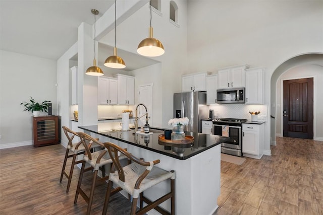 kitchen featuring appliances with stainless steel finishes, sink, white cabinets, a kitchen bar, and hanging light fixtures