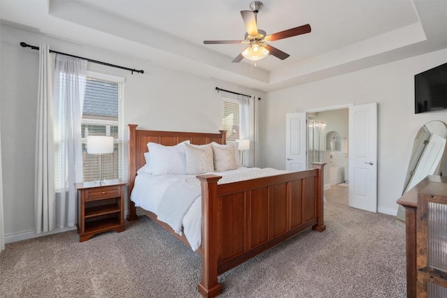 bedroom with ensuite bathroom, light colored carpet, ceiling fan, and a tray ceiling