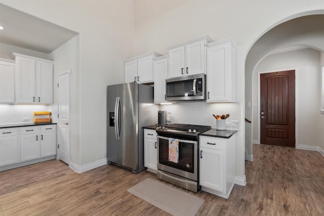 kitchen with appliances with stainless steel finishes, light wood-type flooring, decorative backsplash, and white cabinets