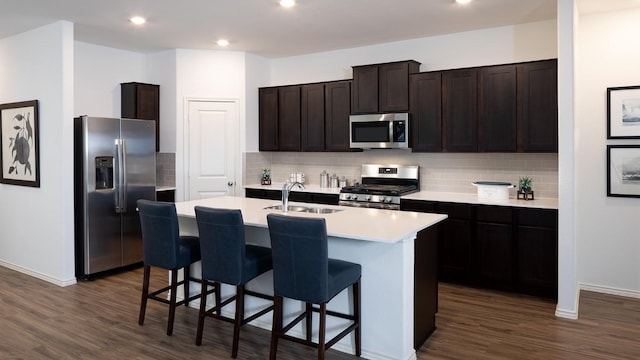 kitchen featuring sink, appliances with stainless steel finishes, dark brown cabinetry, an island with sink, and dark hardwood / wood-style flooring