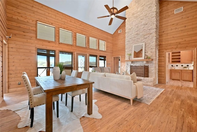 dining room with a stone fireplace, light wood finished floors, wood walls, and visible vents