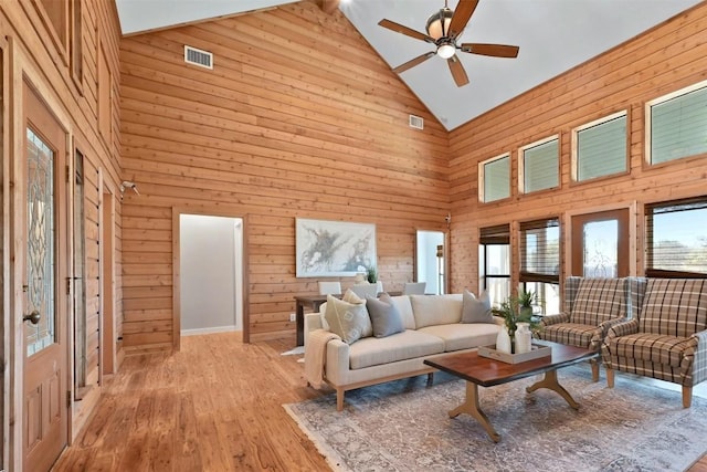 living area with light wood-style flooring, wooden walls, visible vents, and ceiling fan