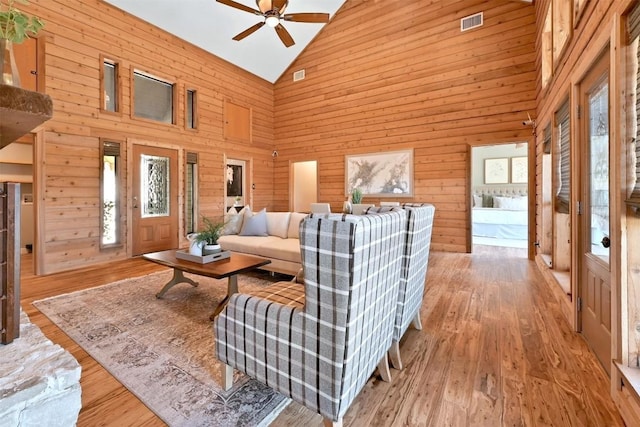 living room with a ceiling fan, high vaulted ceiling, wooden walls, and wood finished floors