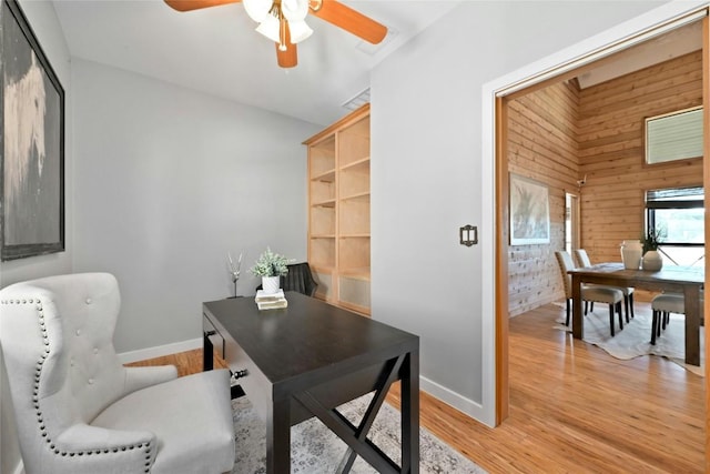 office space featuring light wood-type flooring, wood walls, baseboards, and a ceiling fan