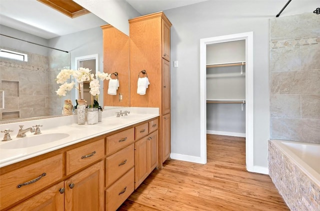 full bath with double vanity, a tile shower, a sink, and wood finished floors