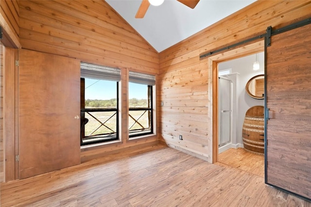 empty room featuring lofted ceiling, a barn door, a ceiling fan, wooden walls, and wood finished floors