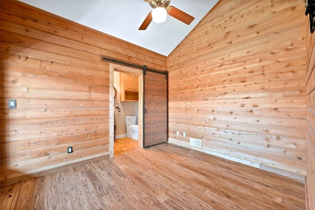 unfurnished room featuring light wood finished floors, lofted ceiling, visible vents, a barn door, and ceiling fan