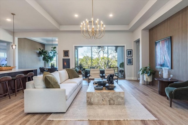 living room with a notable chandelier, light hardwood / wood-style flooring, and a raised ceiling