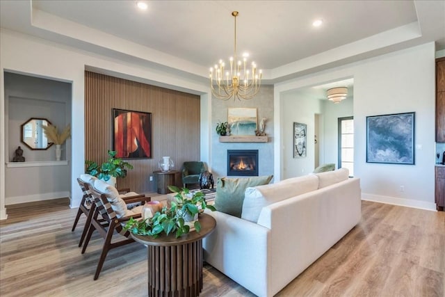 living room with hardwood / wood-style floors, a tray ceiling, a large fireplace, and a chandelier