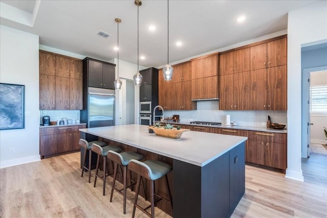 kitchen featuring built in appliances, pendant lighting, a kitchen breakfast bar, and a center island with sink