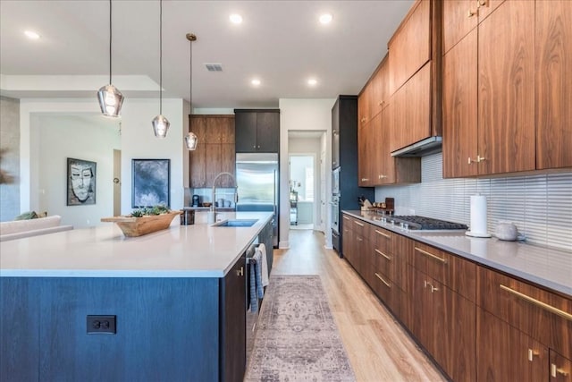 kitchen with light hardwood / wood-style floors, a kitchen island with sink, hanging light fixtures, and backsplash