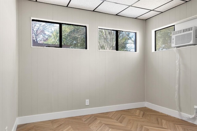 empty room featuring a wall mounted air conditioner, a drop ceiling, and light parquet floors