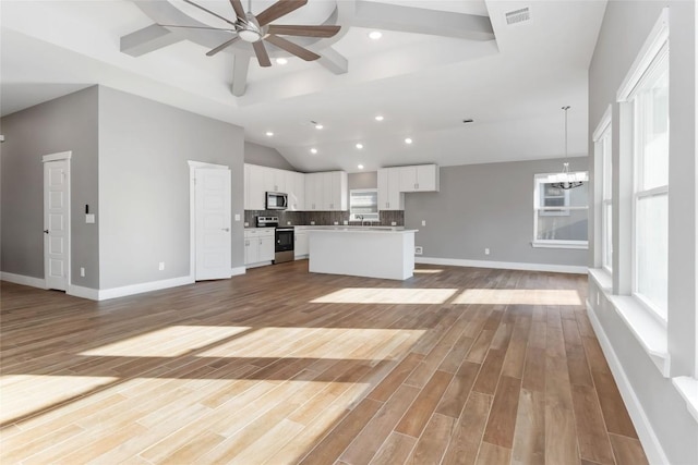 unfurnished living room with a high ceiling, ceiling fan with notable chandelier, and light wood-type flooring