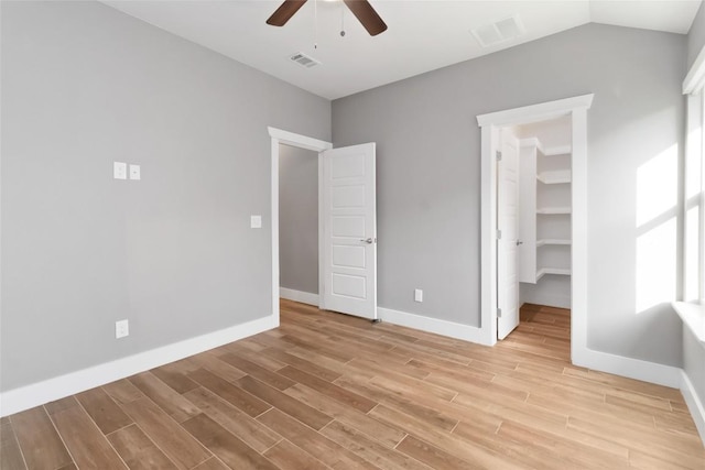 unfurnished bedroom with a walk in closet, vaulted ceiling, a closet, ceiling fan, and light hardwood / wood-style floors