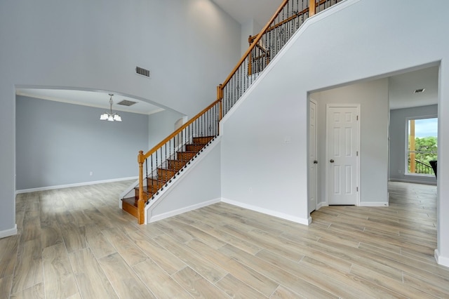 interior space featuring crown molding, a notable chandelier, a towering ceiling, and light hardwood / wood-style floors