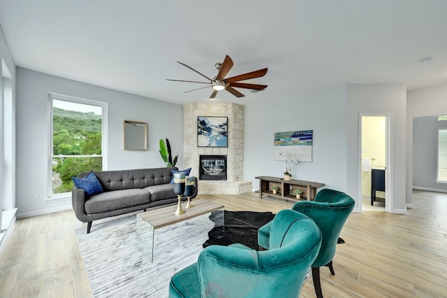 living room featuring ceiling fan, a stone fireplace, and light wood-type flooring