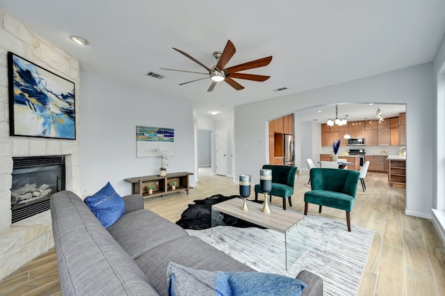 living room featuring a fireplace, ceiling fan with notable chandelier, and light hardwood / wood-style flooring