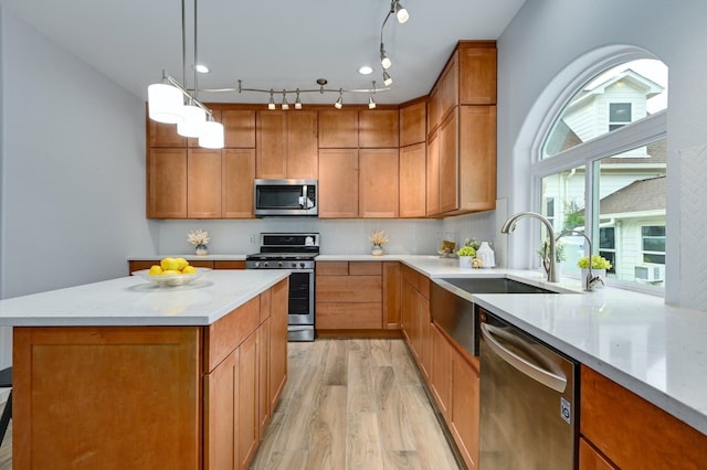 kitchen featuring sink, appliances with stainless steel finishes, pendant lighting, light stone countertops, and light hardwood / wood-style floors