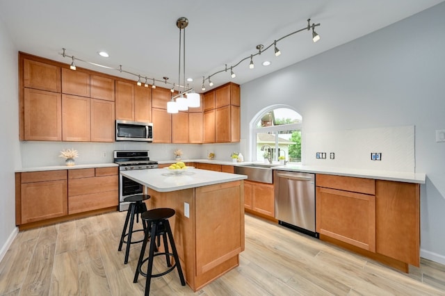 kitchen featuring sink, light hardwood / wood-style flooring, stainless steel appliances, a center island, and decorative light fixtures