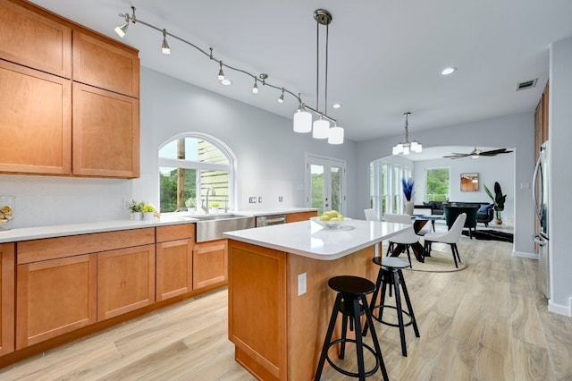 kitchen featuring a kitchen bar, sink, a center island, hanging light fixtures, and light wood-type flooring