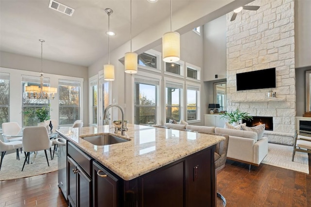 kitchen with sink, a stone fireplace, dark brown cabinetry, light stone counters, and decorative light fixtures