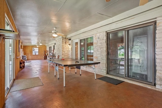 rec room featuring ceiling fan, a wealth of natural light, concrete floors, and wooden walls