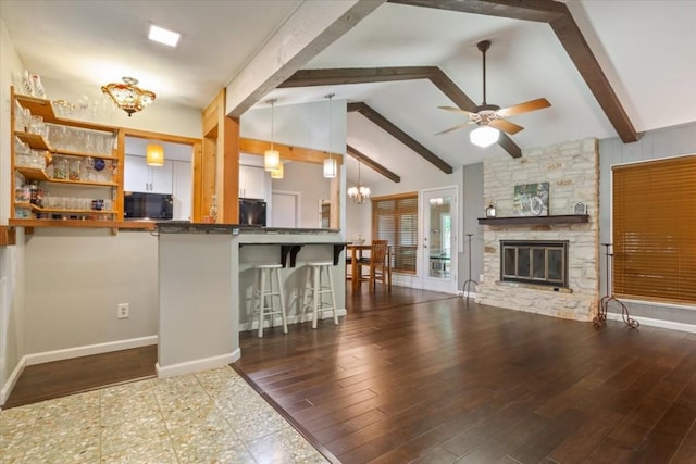 kitchen featuring a breakfast bar, a fireplace, white cabinets, hanging light fixtures, and kitchen peninsula