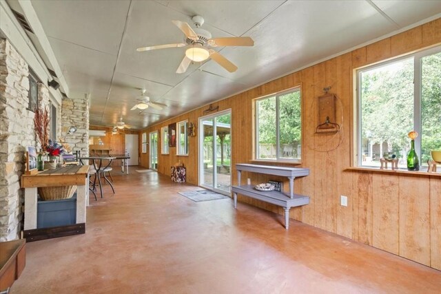 misc room with a fireplace, concrete floors, ceiling fan, and wood walls