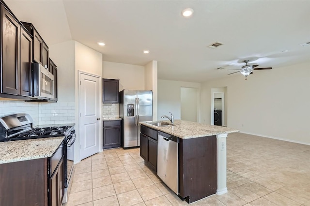 kitchen featuring tasteful backsplash, an island with sink, washer / dryer, light stone counters, and stainless steel appliances