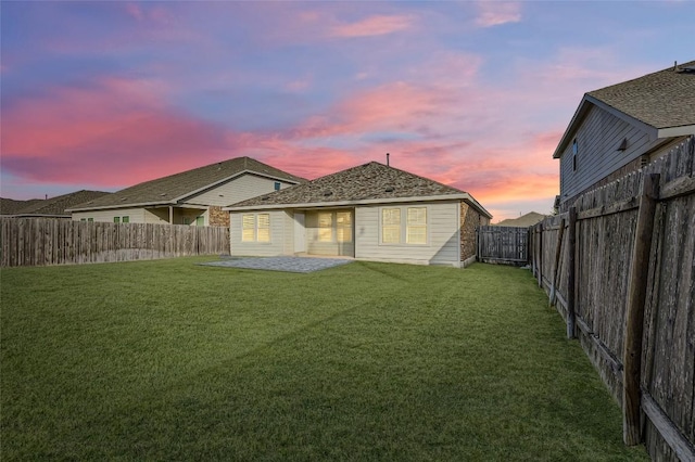 back house at dusk with a patio area and a lawn