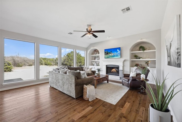 living room with built in shelves, dark hardwood / wood-style floors, and ceiling fan