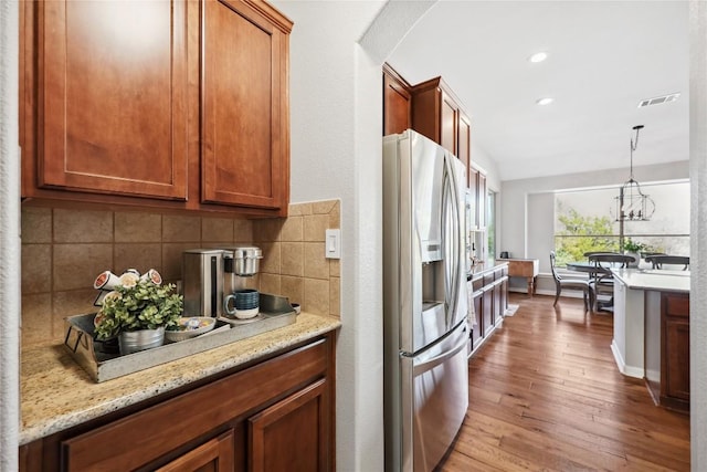 kitchen featuring pendant lighting, backsplash, stainless steel fridge, light stone counters, and light wood-type flooring