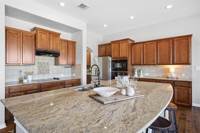 kitchen with sink, a breakfast bar area, a kitchen island with sink, light stone counters, and black appliances