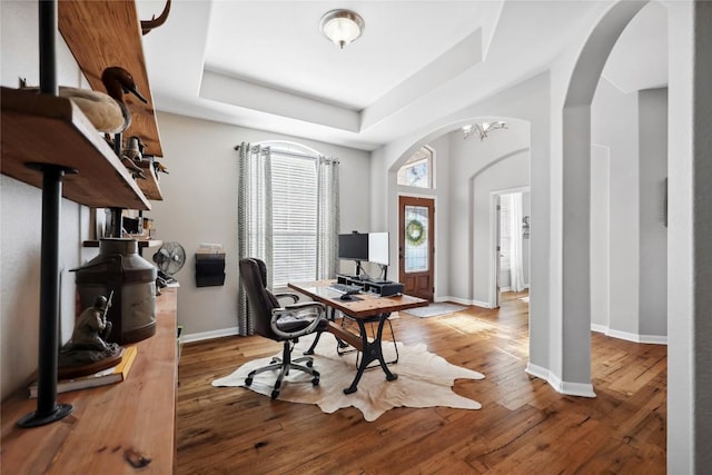 home office with wood-type flooring and a raised ceiling