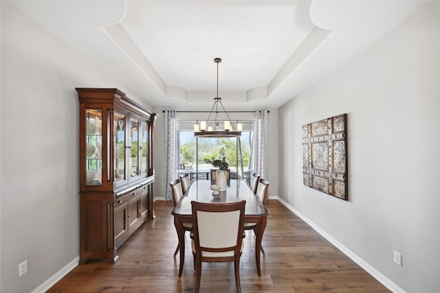 dining space with dark wood-type flooring, a notable chandelier, and a tray ceiling