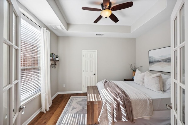 bedroom with dark wood-type flooring, ceiling fan, and a tray ceiling