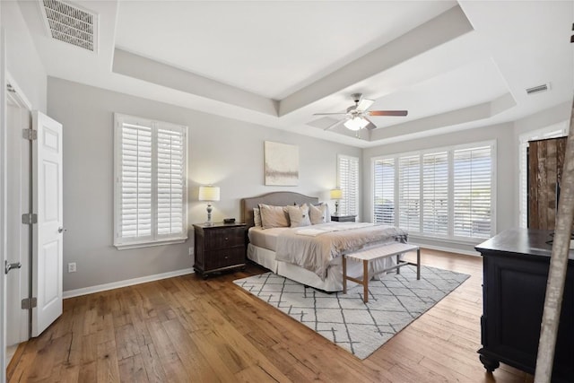 bedroom with wood-type flooring, a tray ceiling, and multiple windows