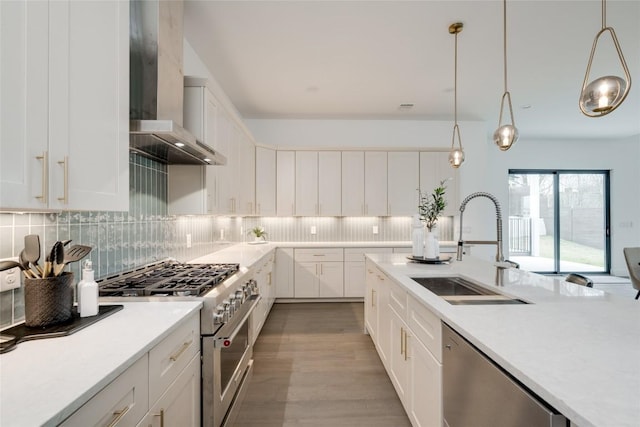 kitchen featuring hanging light fixtures, appliances with stainless steel finishes, wall chimney range hood, and white cabinets