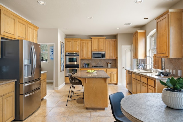 kitchen with sink, stainless steel appliances, a kitchen breakfast bar, tasteful backsplash, and a kitchen island