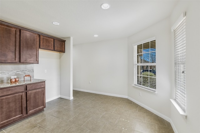 kitchen featuring light stone counters, decorative backsplash, light tile patterned flooring, and dark brown cabinets