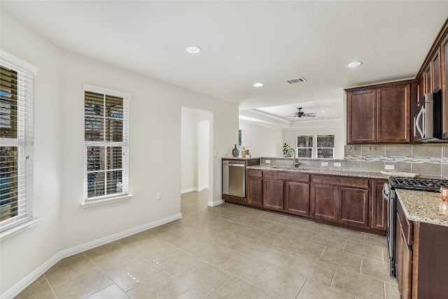 kitchen with dark brown cabinetry, sink, light stone counters, stainless steel appliances, and decorative backsplash