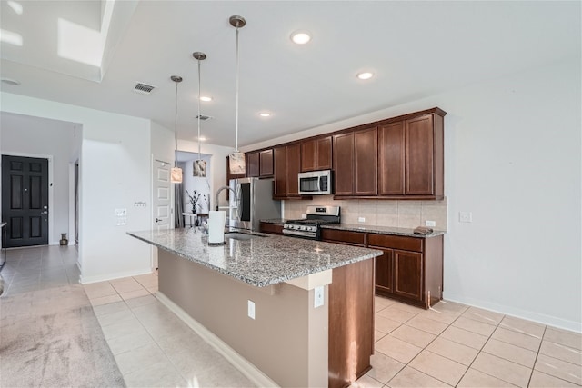 kitchen featuring stone counters, appliances with stainless steel finishes, sink, hanging light fixtures, and a kitchen island with sink