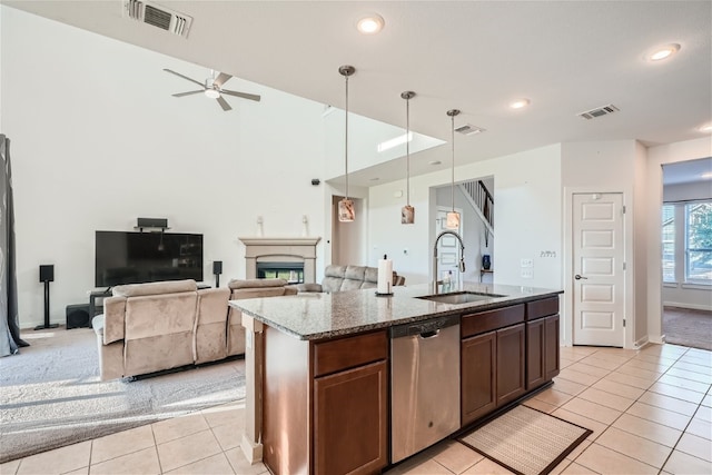 kitchen with pendant lighting, sink, dark stone countertops, an island with sink, and stainless steel dishwasher