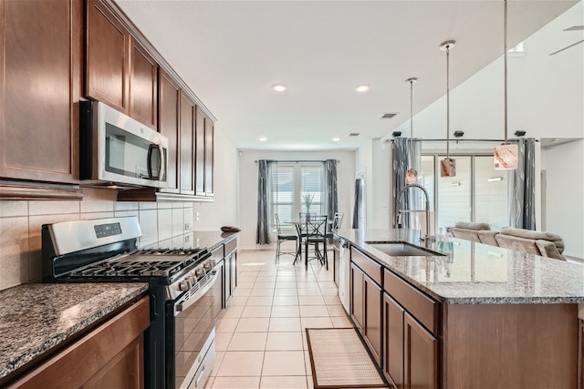 kitchen with sink, a center island with sink, dark stone countertops, pendant lighting, and stainless steel appliances