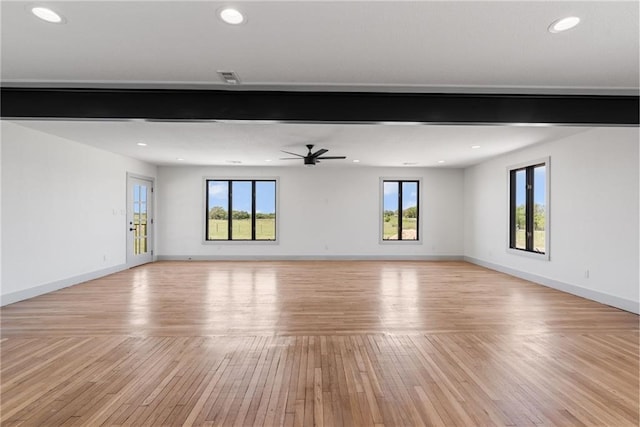 unfurnished living room with beamed ceiling, ceiling fan, a wealth of natural light, and light hardwood / wood-style floors