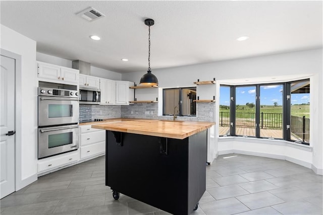 kitchen with wooden counters, appliances with stainless steel finishes, white cabinetry, a center island, and decorative light fixtures