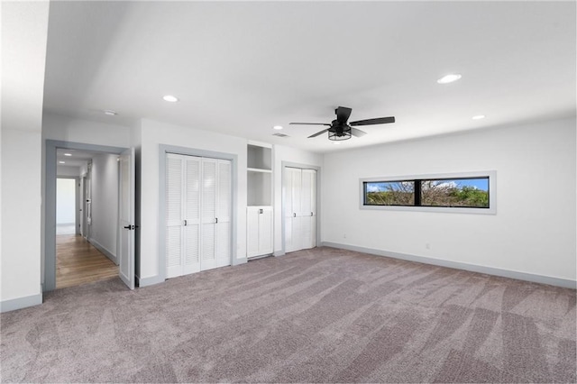 unfurnished bedroom with two closets, light carpet, and ceiling fan