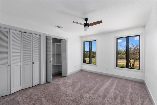 unfurnished bedroom featuring ceiling fan, light colored carpet, and two closets