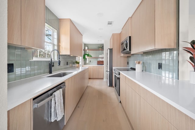 kitchen featuring sink, backsplash, stainless steel appliances, light hardwood / wood-style floors, and light brown cabinetry