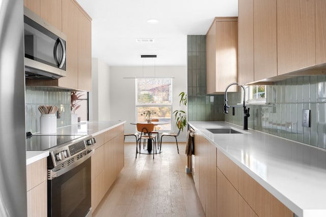 kitchen with stainless steel appliances, decorative light fixtures, light brown cabinetry, and sink